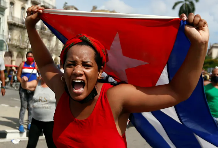 A Cuban woman shouting, wearing read and carrying a Cuban flag.