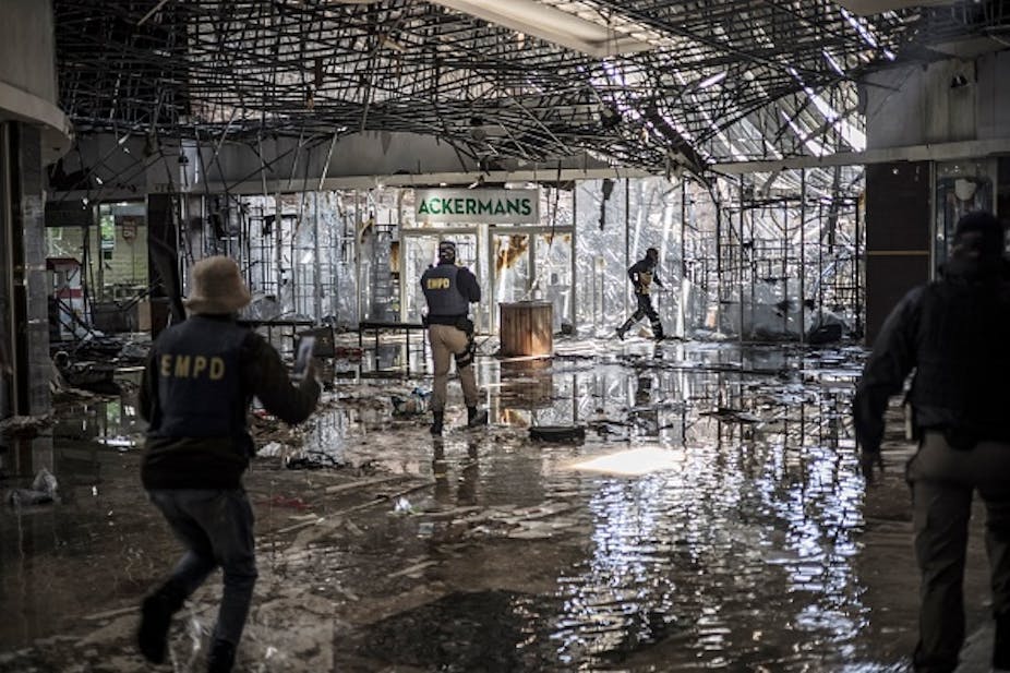 Interior of a building with damaged ceiling and water on the floor; people wearing police bulletproof vests
