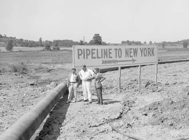 Three men next to a bend in a large pipeline.