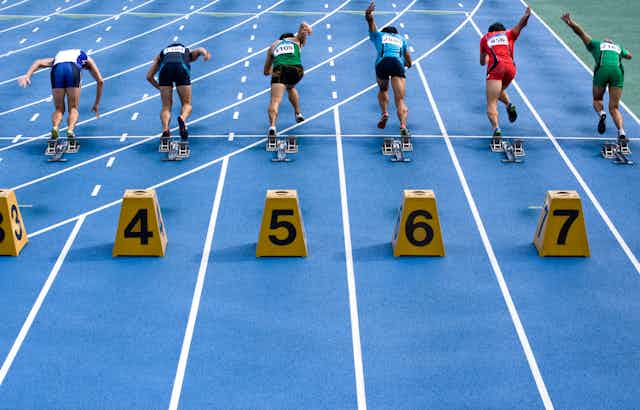 Runners leaving the starting block on a track with lane numbers behind them.