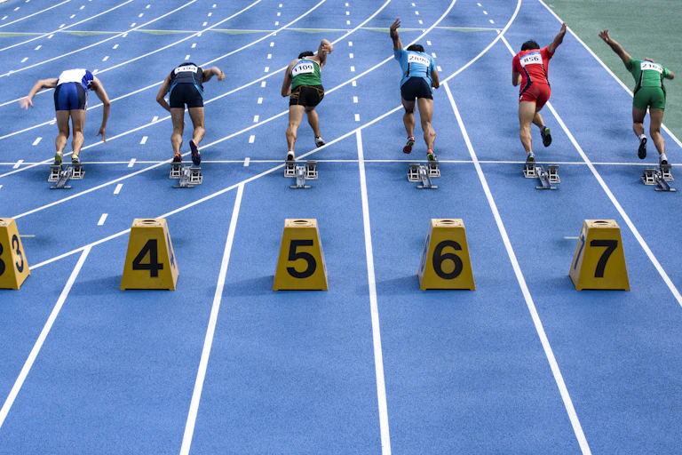 Runners leaving the starting block on a track with lane numbers behind them.