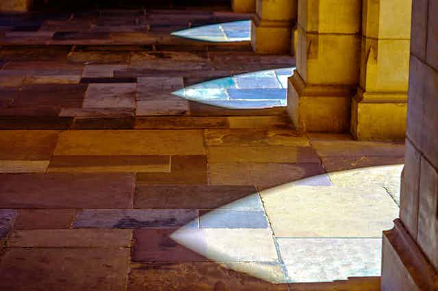 Sunlight falls onto slate tiles through stone archways at the University of Melbourne in Australia