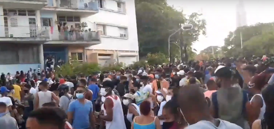 Large crowd outside apartment block, most wearing COVID masks.