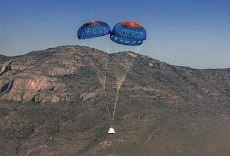 Image of Blue Origin's New Shepherd spacecraft landing with parachutes.