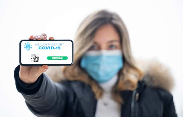 Masked woman holds phone showing COVID-19 passport.