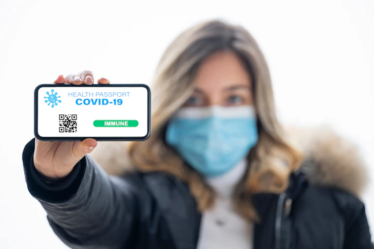 Masked woman holds phone showing COVID-19 passport.