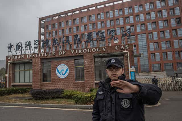 A security guard waves away a photographer outside the Wuhan Institute of Virology.