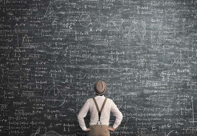 A man consults a large blackboard of equations