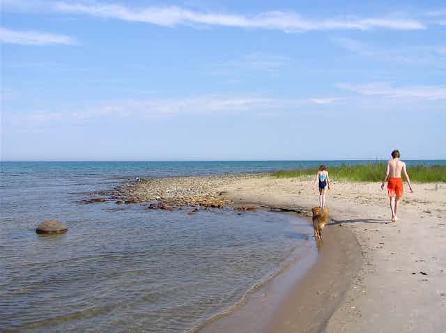 Two people walk along a spit of sand.