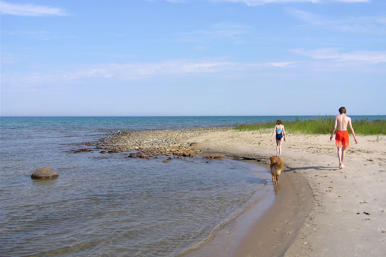 Two people walk along a spit of sand.