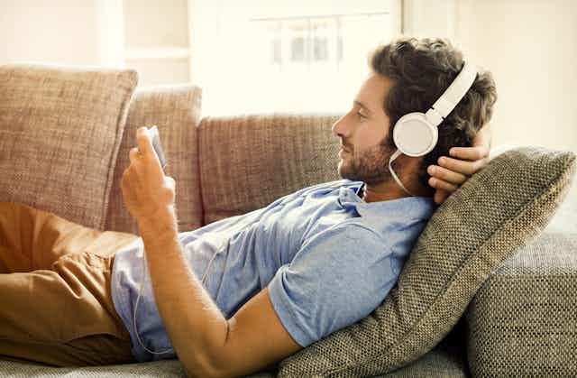 A man relaxing on a couch with headphones on, watching a video on his phone