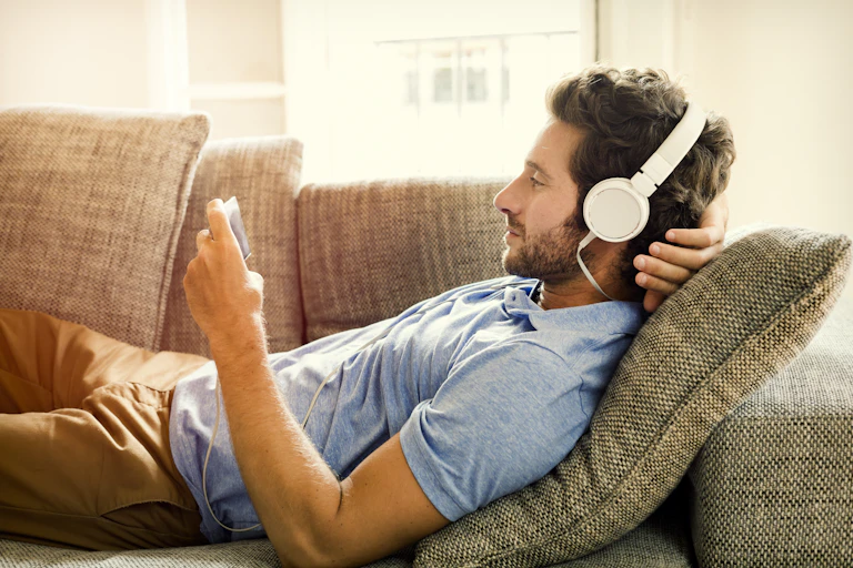 A man relaxing on a couch with headphones on, watching a video on his phone