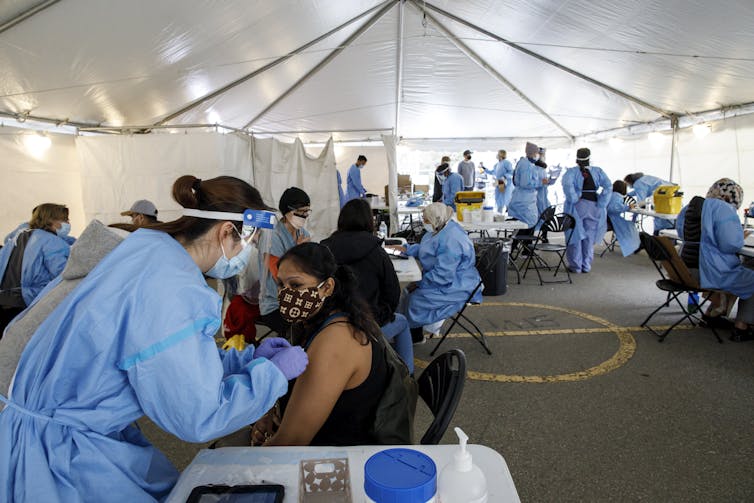 People in masks are vaccinated by health-care workers in protective gear inside a tent