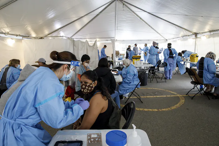 Los códigos postales no deberían determinar la protección: lo que revela el RSV sobre la equidad en las vacunas en Canadá 2 Las personas con máscaras son vacunadas por trabajadores sanitarios con equipo de protección dentro de la tienda.