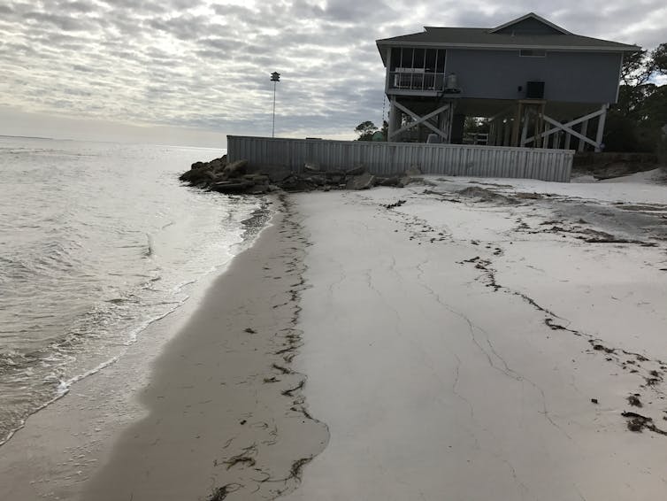 House fronted by sea wall extending into the ocean.