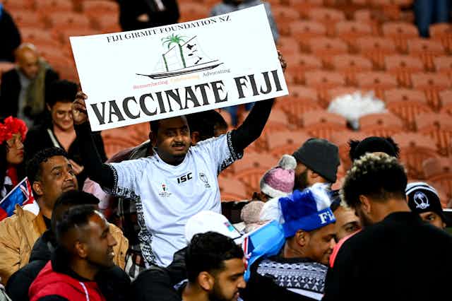 Rugby fan holdin sign saying 'vaccinate Fiji'