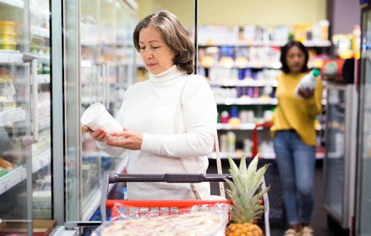 Woman in supermarket looks at the packaging of a yoghurt container.