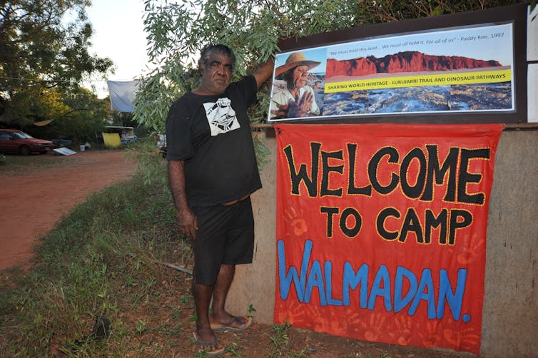man stands next to sign at Aboriginal camp