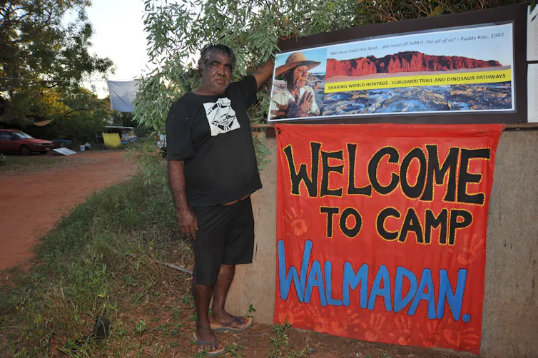 man stands next to sign at Aboriginal camp