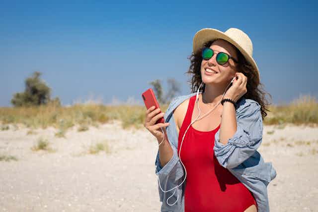 Una mujer en la playa escuchando un audio a través del móvil.