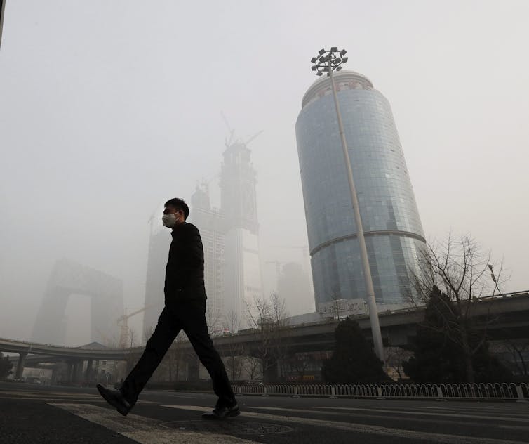 A man wearing a mask walks in smog.