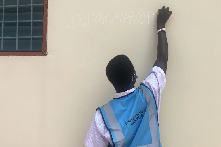 A man wearing an official census waistcoat writes on a wall