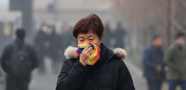 A woman covers her mouth with her scarf as she walks in smog.