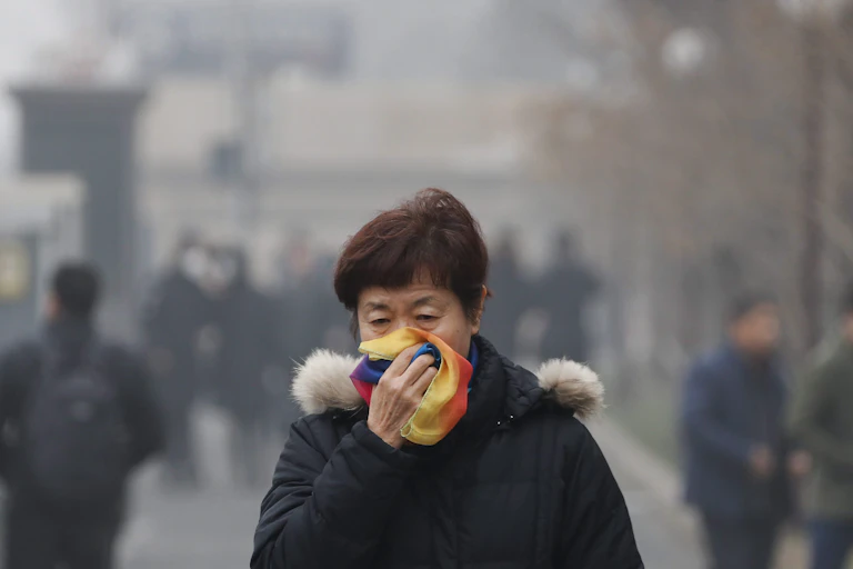 A woman covers her mouth with her scarf as she walks in smog.
