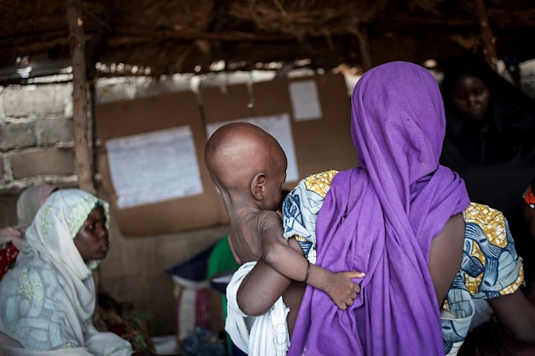 A woman wearing a head wrap holding a baby who appears to be underweight