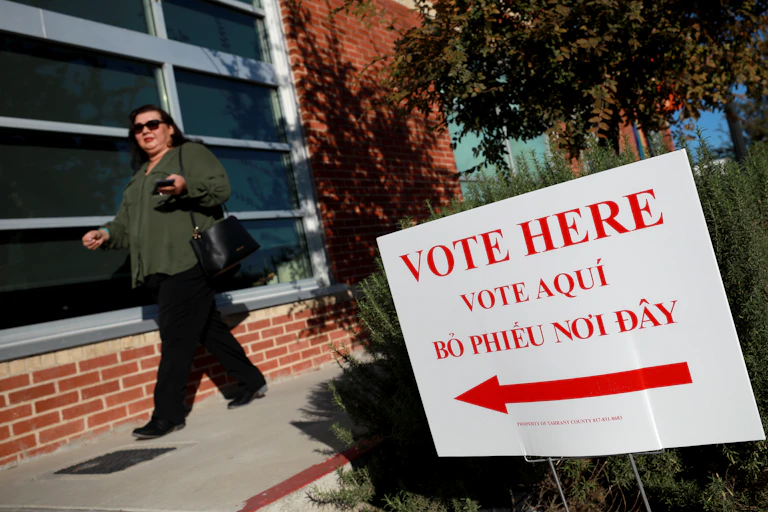 A voter walking past a sign that says "Vote here" in English and two other languages.