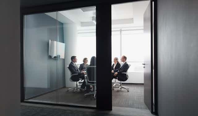 People in business attire gather in a room, with a door that's open