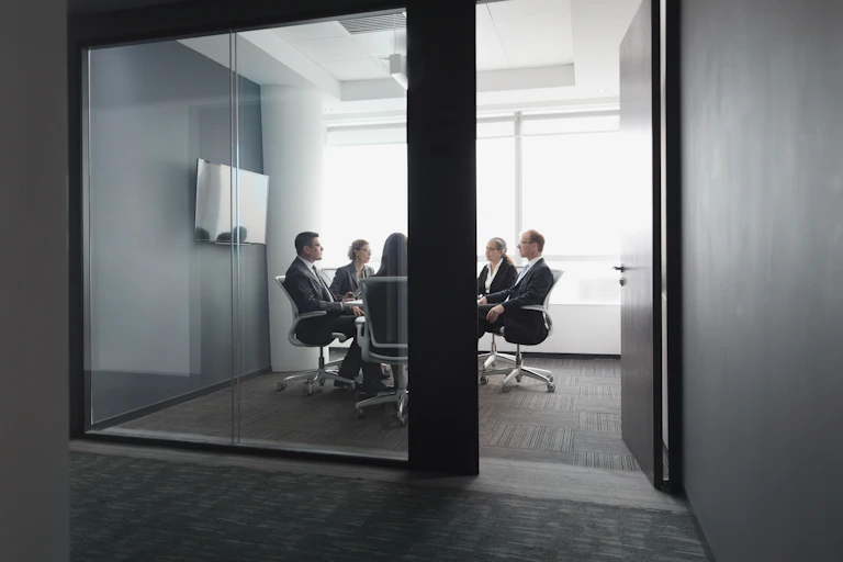 People in business attire gather in a room, with a door that's open