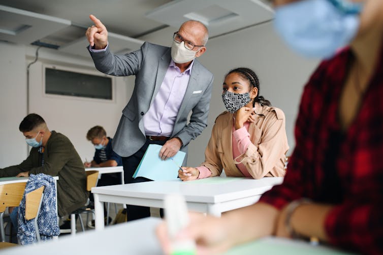 Masked teacher explains a point to masked student