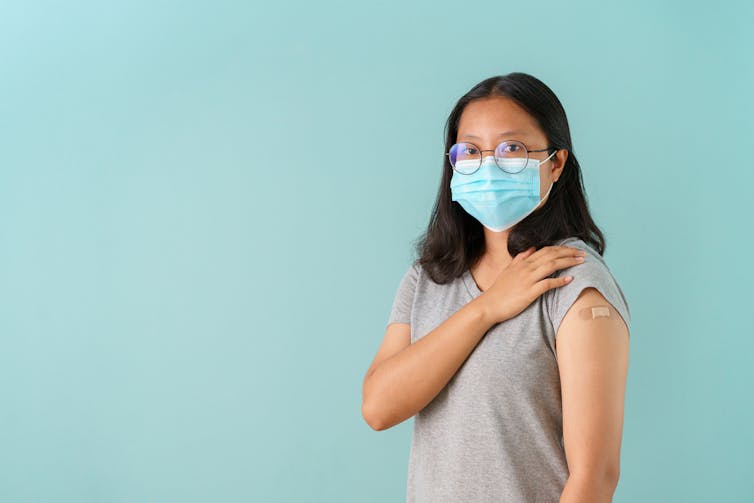 Teenager wearing face mask showing bandaid on shoulder just vaccinated