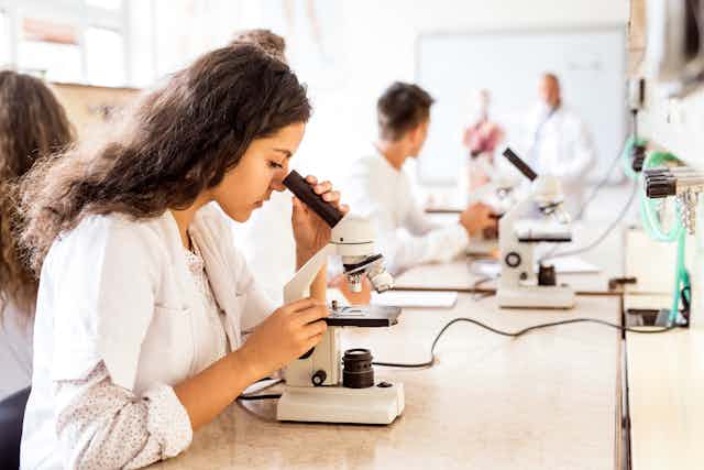 Senior students in lab coats looking through microscopes.
