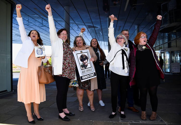 A group of seven people looking joyous with their fists in the air. One holds a sign with a photo of her family member and the word 'innocent'.