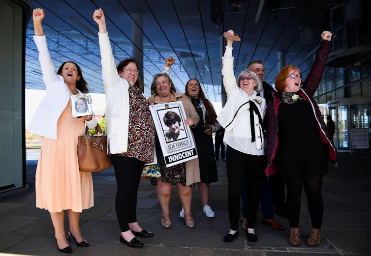 A group of seven people looking joyous with their fists in the air. One holds a sign with a photo of her family member and the word 'innocent'.