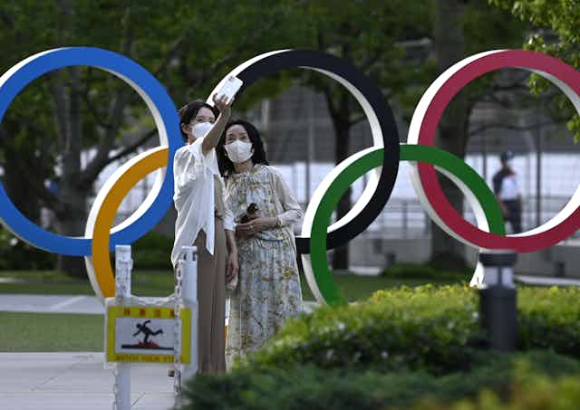Two visitors pose for selfie next to Olympic rings.