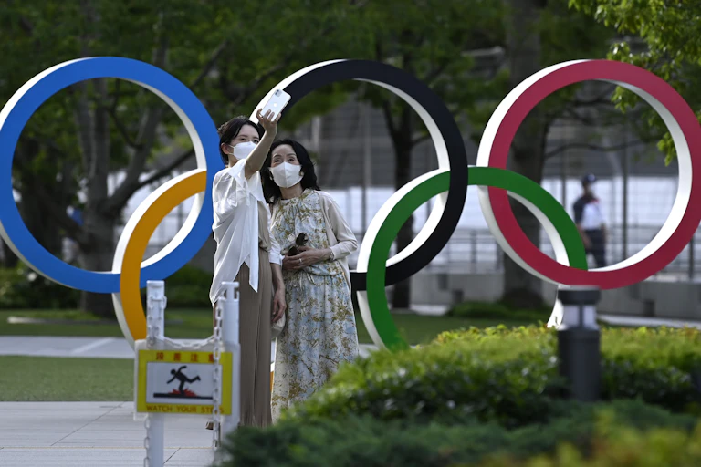 Two visitors pose for selfie next to Olympic rings.