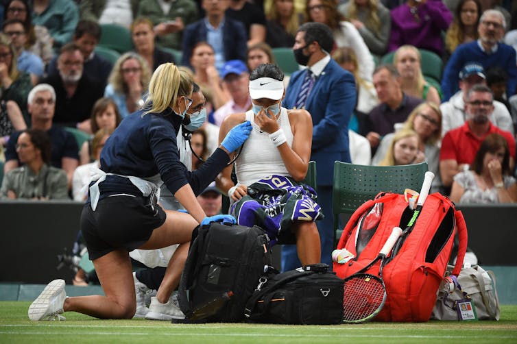Healthcare professionals attend to tennis player Emma Raducanu during a Wimbledon match