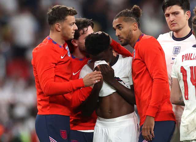 English player Bukayo Saka is comforted by teammates after missing a penalty in the England v Italy final of the Euros 2020