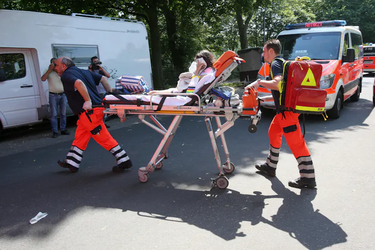 Paramedics lead a patient to an ambulance on a stretcher.