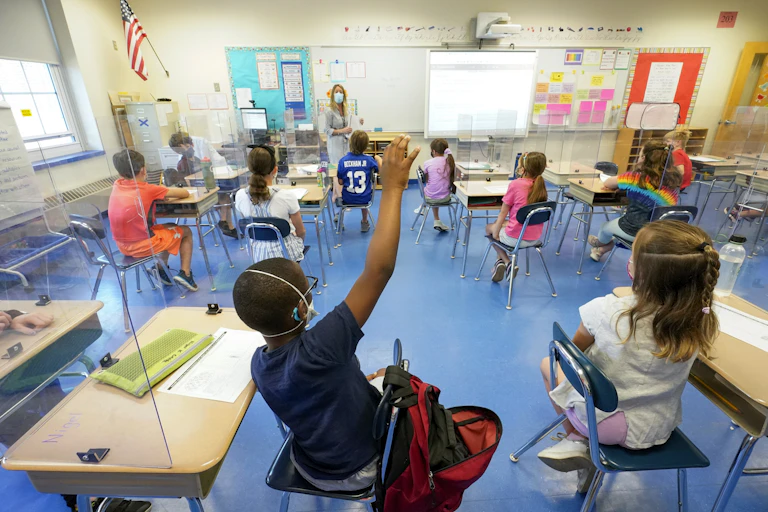 Children in a classroom; one is raising his hand.