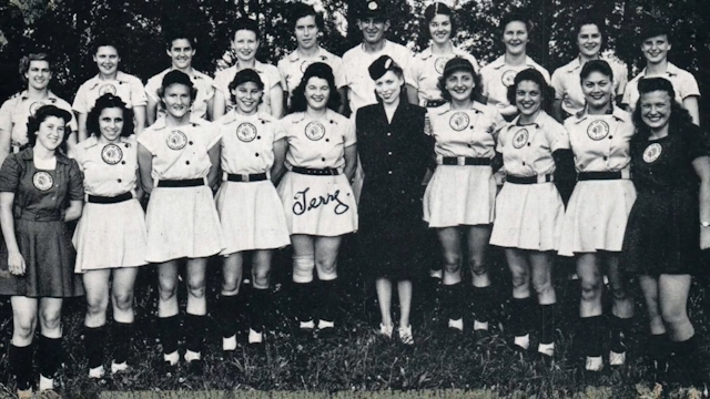 Two rows of women in vintage skirted baseball uniforms.