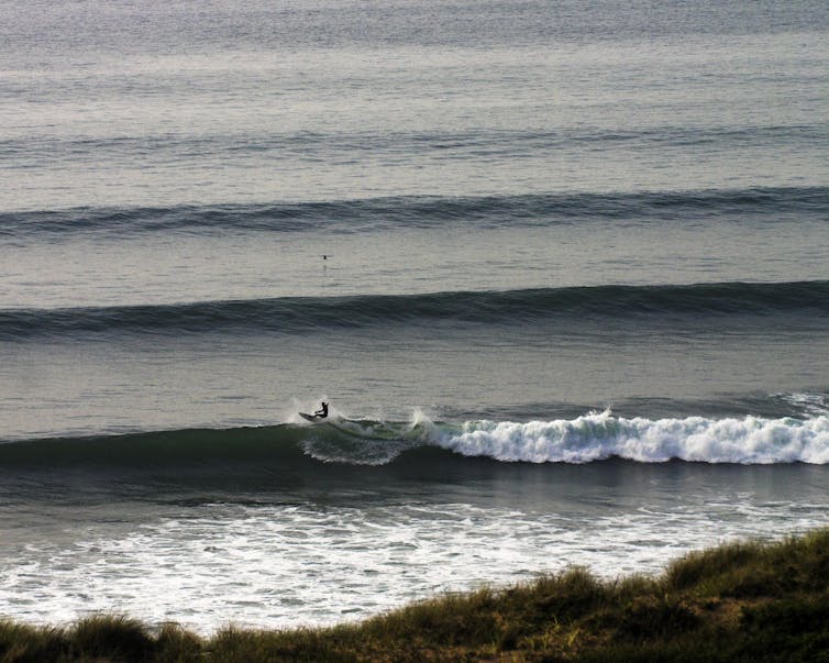 Lines of waves out to sea with a surfer in the foreground.