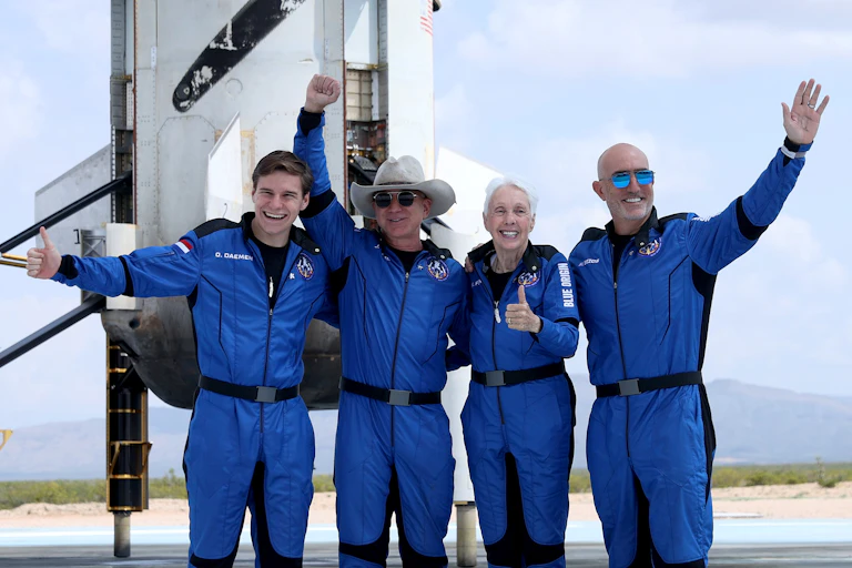 Four white people wearing space suits take a photo in front of a spaceship.