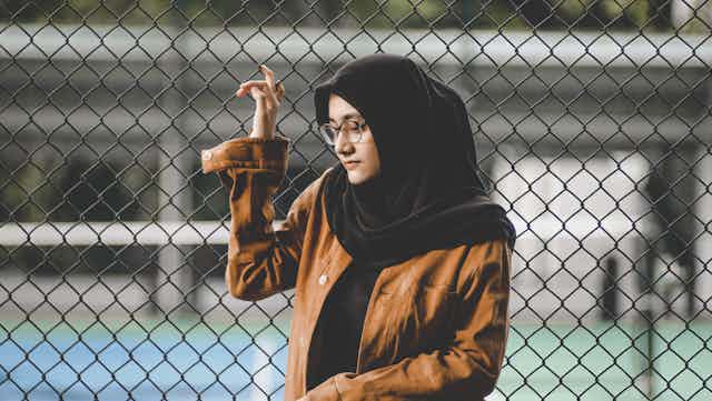 A girl in a hijab stands at a fence. 
