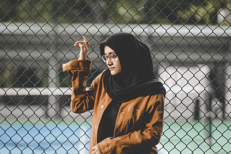 A girl in a hijab stands at a fence.