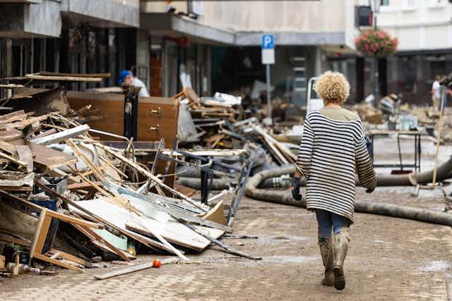 A woman filthy with mud walks past a pile of rubble.