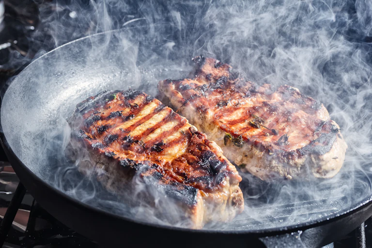 Smoke rising from frying pork steaks